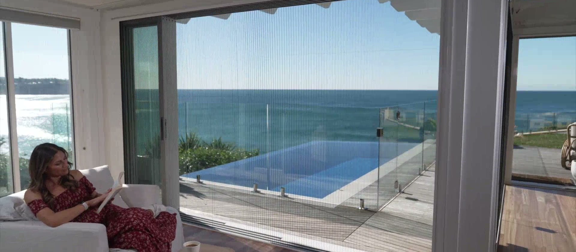 Pleated screen drawn across a full-width opening onto a pool and the sea, the room in ordinary use behind it