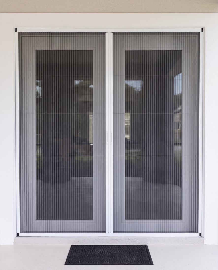 Pleated screen drawn fully across a double patio door, the two halves meeting at a centre bar